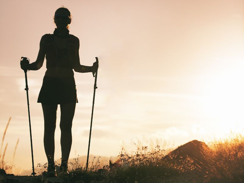 Femme avec des bâtons de trail au coucher du soleil